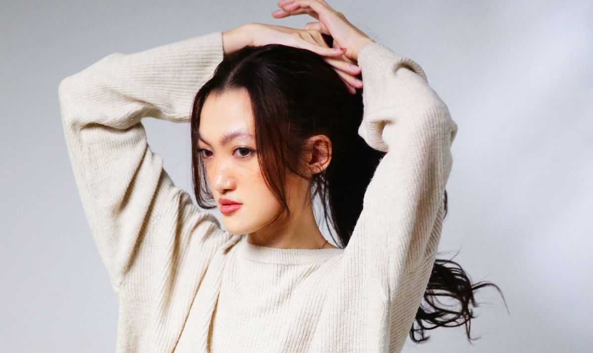 alt="Penyanyi Meha mengikat rambut sambil mengenakan sweater krem dalam pemotretan promosi single Ada Rasa bernuansa retro pop tahun 2025"